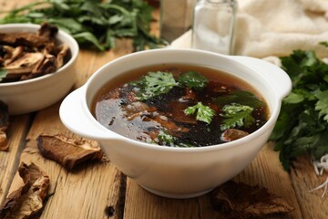Tasty soup with mushrooms and parsley in bowl on wooden table, closeup