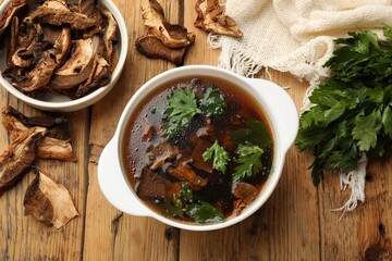 Tasty soup with mushrooms and parsley in bowl on wooden table, flat lay