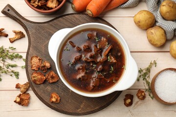 Tasty soup with mushrooms in bowl and products on light wooden table, flat lay