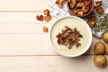 Tasty cream soup, thyme and dry chanterelle mushrooms on light wooden table, flat lay. Space for text