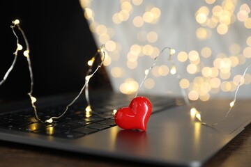 Online dating site. Decorative heart and laptop on table against blurred lights, closeup. Bokeh...