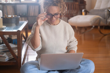 Young woman with curly hair working at home on her laptop, sitting at a table in a cozy modern...
