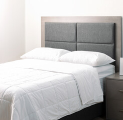 Elegant bed with grey fabric padded headboard and white pillows, duvet, and sheets, placed next to...