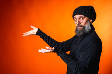 Expressive man with beard and glasses points with both hands on vibrant orange background. Surprise, attention, direction, recommendation