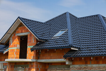 A metallic tiled roof is being installed on a residential building with brick walls, showcasing modern construction techniques