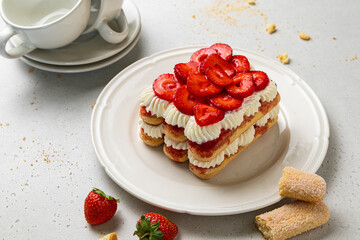 Tradition Italian layered dessert tiramisu with mascarpone cream and ladyfingers biscuits on a white background. Strawberry tiramisu cake. Summer easy no bake dessert. Home cooking. Selective focus.