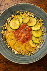 Gourmet vegetarian and vegan carpaccio with sliced zucchini and yellow squash over a tomato puree, sprinkled with mixed seeds; a healthy, light appetizer for fine dining served on a rustic plate.