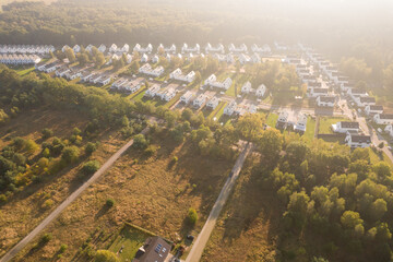 Aerial view of a modern residential development with white houses next to a forest at sunrise