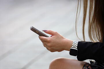 Smartphone in female hands on a street. Girl sitting on a bench in summer city and using mobile...