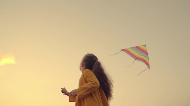 little girl daughter launches a kite high into the sky, children's play outdoors, kid dreams of flying, colorful rainbow toy, child has fun in game in nature, happy family, catching wind with his hand