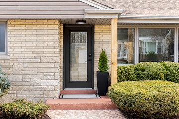 A front door detail with a yellow brick and stone siding, black front door with pattern frosted...