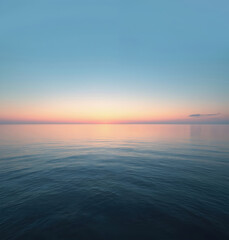 Obraz premium Serene ocean sunset at dusk with calm water. Deep blue sea meets light orange sky, creating stunning contrast. Horizon line merges with sky in distance, creating peaceful atmosphere.