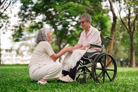 Asian elderly couple supporting each other outdoors park happy retirement life senior care wheelchair husband wife mature adult bonding connection