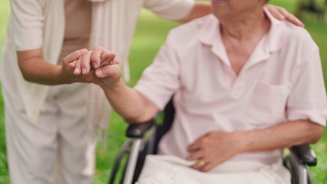 Asian senior couple support healthcare holding hands wheelchair park garden elderly care retirement wellbeing lifestyle aging partnership