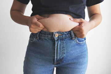 Closeup of woman pinching belly fat in jeans and black crop top, body fat and stretch marks on...