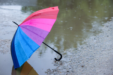 Colorful umbrella on wet asphalt under heavy rain. Space for text