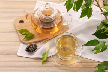 Tasty green tea in glass cup, teapot, brew and leaves on wooden table, above view