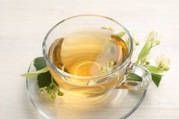 Fresh linden tea in cup and flowers on white wooden table, closeup