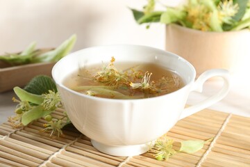 Fresh linden tea in cup and flowers on white table, closeup