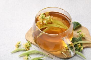 Fresh linden tea in cup and flowers on light grey table, closeup. Space for text
