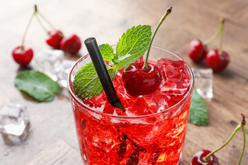 Tasty cherry soda with ice cubes, berries and mint in glass on wooden table, closeup