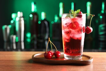 Tasty cherry soda water with ice cubes, berries and mint in glass on table against blurred green...