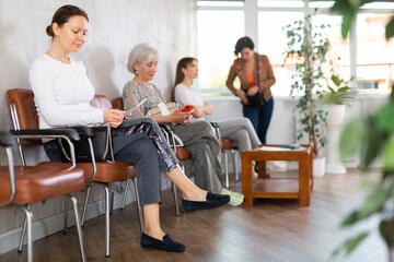 Female applicant is waiting for interview and is sitting in line with other women, holding resume...