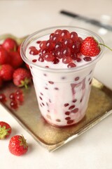 Tasty milk bubble tea in plastic cup and strawberries on white table, closeup