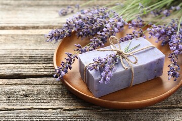 Aromatic soap bar and lavender flowers on wooden table, closeup