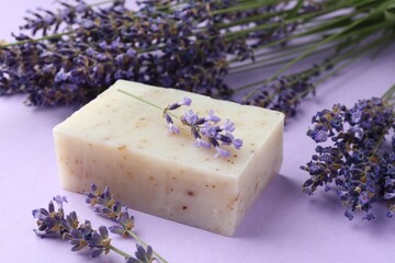 Aromatic soap bar and lavender flowers on violet background, closeup