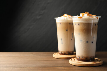 Tasty milk bubble tea in plastic cups on wooden table, closeup. Space for text
