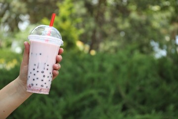 Woman with tasty milk bubble tea in plastic cup outdoors, closeup. Space for text