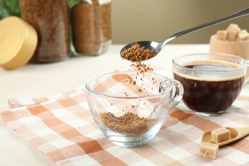 Putting instant coffee into cup at light table, closeup