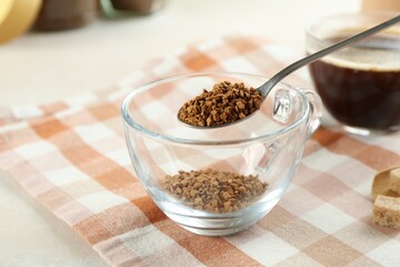 Putting instant coffee into cup at light table, closeup