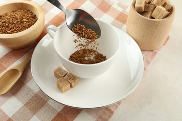 Putting instant coffee into cup at light table, closeup