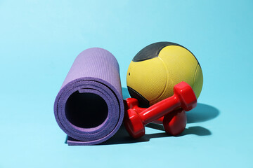 Medicine ball, fitness mat and dumbbells on light blue background