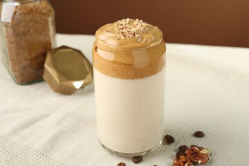 Delicious dalgona coffee in glass, beans, walnuts and granules on table, closeup