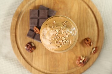 Delicious dalgona coffee in glass, pieces of chocolate and walnuts on table, top view