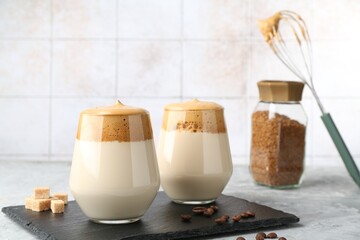 Delicious dalgona coffee in glasses, brown sugar, beans, whisk and granules on grey table, closeup