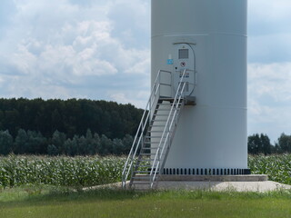 Wind turbine base with metal staircase and access platform surrounded by agricultural corn field