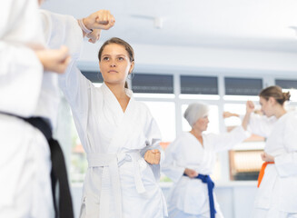 Two young women in kimonos practicing karate techniques in group at gym