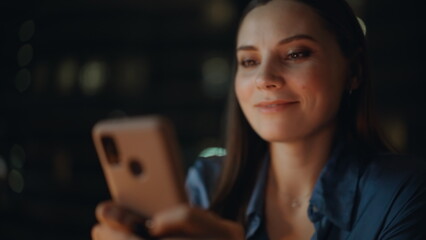 Joyful woman browsing smartphone message at dark room closeup. Smiling lady