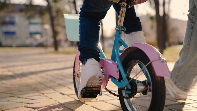 little child turns wheels on a two-wheeled bicycle, mother helps kid learn to control a bicycle, baby steers keeping balance, wheel and leg close-up, walk in the park mom and baby, road travel game.