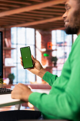 Happy man at home using green screen phone to browse social media website, looking at memes. Jolly person in apartment looking at funny content online on chroma key smartphone