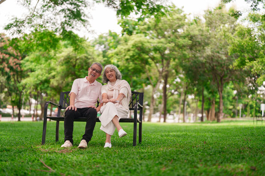 Asian older couple happy smile sitting park bench enjoy retired golden years relaxing nature senior lifestyle leisure outdoor activity together love
