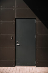 Modern dark door on a textured wall with geometric shadows in bright sunlight