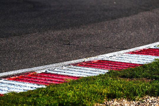Close-up of a red and white rumble strip on a motorsport racing track. Asphalt surface with visible wear and textured road lines. Ideal for themes of racing, speed, automotive design, road safety