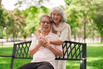 Asian older couple enjoy retirement relaxation on park bench warm embrace share happy moments...