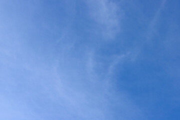 A vibrant blue sky featuring thin and sparse white cirrus clouds, spreading subtly, creating an atmosphere of lightness and tranquility.