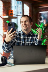 Joyous freelancer in home office sitting at desk in front of laptop, greeting colleagues in...